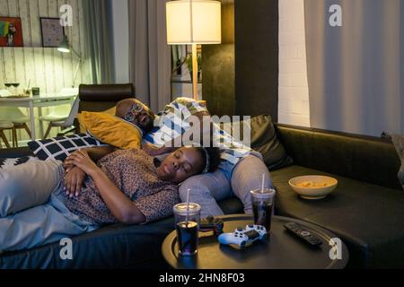 Giovane coppia africana che dormiva insieme sul divano in soggiorno, si stancavano dopo aver giocato il videogioco Foto Stock