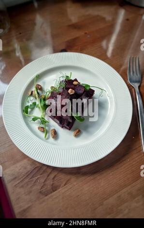 Insalata di barbabietole cotte in casa con noci e germogli di piselli verdi sul piatto bianco, luce del sole Foto Stock