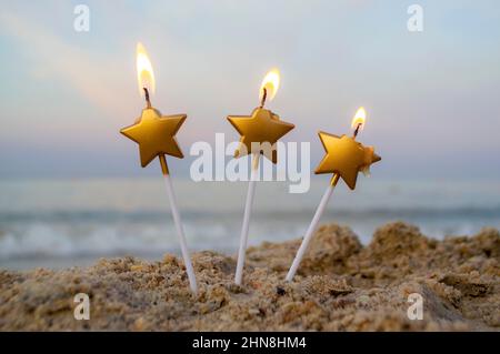 Tre candele di forma di stella bruciano in sabbia sulla spiaggia sullo sfondo Foto Stock