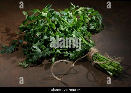 Prezzemolo su sfondo tavolo in legno. Vista dall'alto della pianta di prezzemolo fresco e crudo. Prezzemolo fonte indispensabile di vitamine A, C, K, B1, B2, PP, E, C. Foto Stock