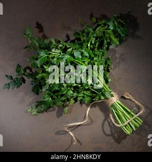 Prezzemolo su sfondo tavolo in legno. Vista dall'alto della pianta di prezzemolo fresco e crudo. Prezzemolo fonte indispensabile di vitamine A, C, K, B1, B2, PP, E, C. Foto Stock