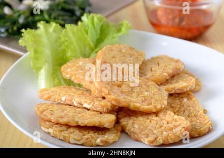 Fritto Tempe / tempeh in piatto bianco, con una fetta di lattuga come guarnitura. Tempe, cibo asiatico a base di soia Foto Stock