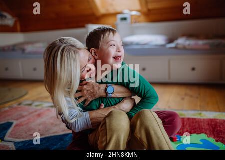 Ragazzo felice con sindrome di Down seduto a terra e abbracciato con la nonna a casa Foto Stock
