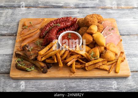 set di spuntini: salsicce, patate fritte, palle di carne, gnocchi, basturma su un tagliere su sfondo grigio di legno. Vista laterale, primo piano. Foto Stock