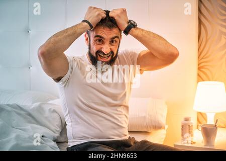 persona con qualche tipo di problema seduta sul letto e tirando i capelli Foto Stock