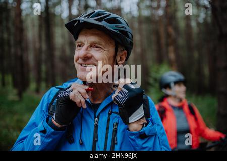 Motociclisti senior che mettono il casco da ciclismo all'aperto nella foresta nel giorno d'autunno. Foto Stock