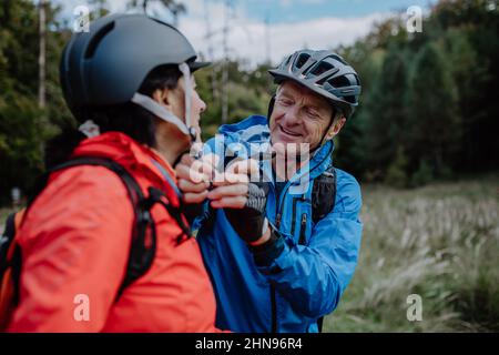 Motociclisti senior che mettono il casco da ciclismo all'aperto nella foresta nel giorno d'autunno. Foto Stock