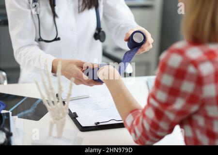 Un medico in clinica bende il polso della donna con una fascia elastica Foto Stock