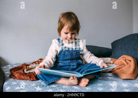 Il bambino legge il suo libro preferito a casa. Il bambino guarda le immagini nelle fiabe. Foto Stock