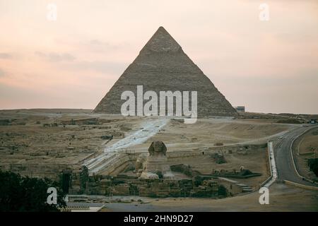 Grande sfinge e piramidi sotto il sole luminoso. Vista dell'altopiano di Giza con le grandi piramidi e la sfinge in serata al tramonto Foto Stock