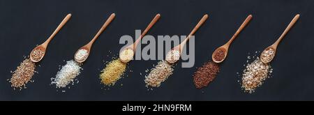 Set di cereali e riso diversi in cucchiaio di legno su sfondo nero, vista dall'alto Foto Stock