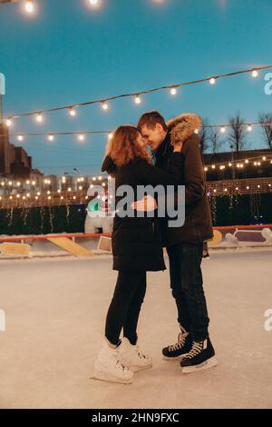 Una giovane coppia innamorata sta pattinando su una pista di pattinaggio, abbracciando e sorridendo. Foto Stock