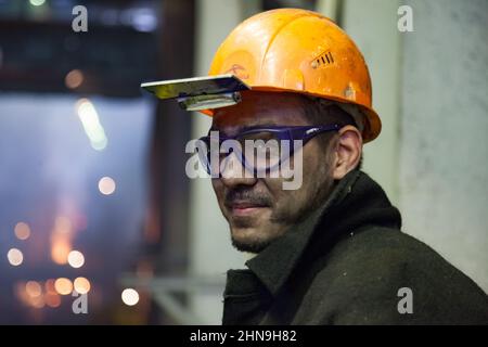 Temirtau, Kazakistan - 08 giugno 2012: Fonderia Arcelor Mittal. Produzione di acciaio. Sorridente metallurgista giovane con volto sporco in hardhat arancione e pr Foto Stock