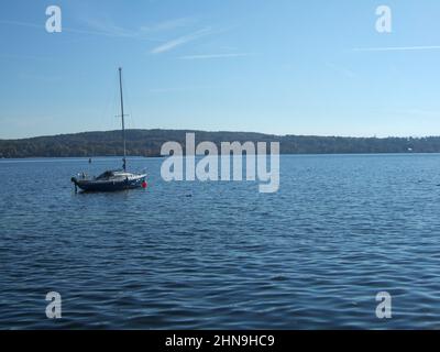 Una barca a vela sul lago Ammersee in Baviera sotto il cielo azzurro e soleggiato con la riva boschiva sullo sfondo Foto Stock