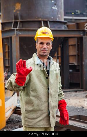 Temirtau, Kazakhstan - 08 giugno 2012: Impianto di metallurgia Arcelor Mittal. Ritratto della saldatrice in guanti di gomma reg. Elmetto giallo con logo di Troy compa Foto Stock