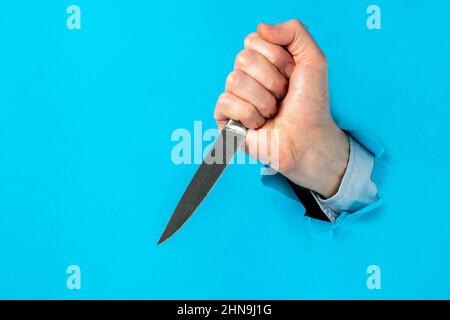 L'uomo si è rotto attraverso il muro di carta con un coltello. La lama passava attraverso la parete della carta. Concetto di aggressione. Foto Stock