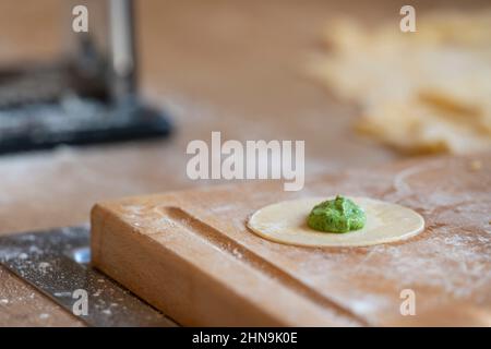 piatto da forno rotondo con porzione di spinaci per gnocchi tirolesi originali schlutzkrapfen in cucina con tavola di legno piena di farina Foto Stock