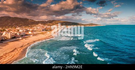 Spettacolare vista aerea panoramica dell'iconica cittadina turistica di Sarti e della famosa spiaggia di sabbia lunga e vuota al tramonto con onde alte. Vacanza su Halkidiki Foto Stock