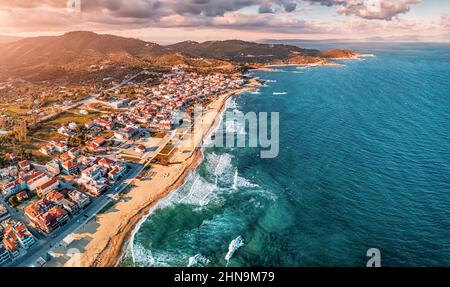 Spettacolare vista aerea panoramica dell'iconica cittadina turistica di Sarti e della famosa spiaggia di sabbia lunga e vuota al tramonto con onde alte. Vacanza su Halkidiki Foto Stock