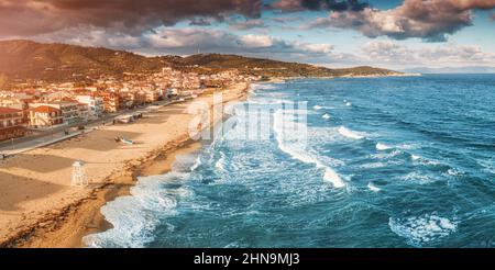 Spettacolare vista aerea panoramica dell'iconica cittadina turistica di Sarti e della famosa spiaggia di sabbia lunga e vuota al tramonto con onde alte. Vacanza su Halkidiki Foto Stock