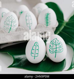 Disegni uova con foglie tropicali. Uova tropicali di pasqua concetto. Piante di monstera verde e foglie di palma tropicali dipinte su guscio d'uovo. I disegni di Pasqua sull'idea della conchiglia dell'uovo Foto Stock