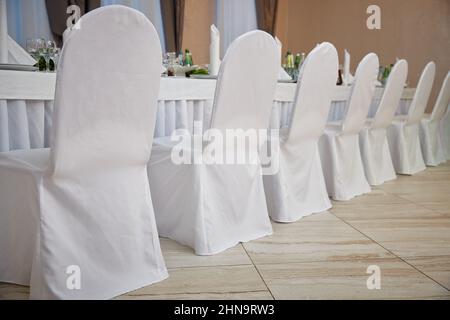 Sedie in coperte bianche in un ristorante vicino ad un tavolo set. Matrimonio Foto Stock