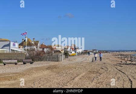 Pevensey Bay views East Sussex Inghilterra UK - Walkers sulla spiaggia con case che si affacciano sul lungomare Foto Stock