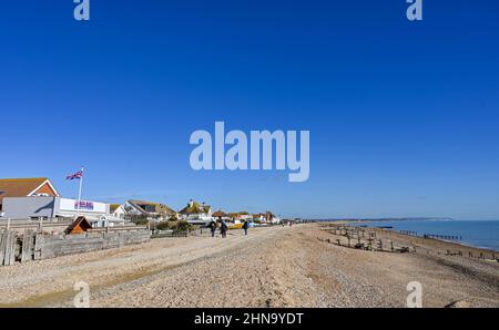 Pevensey Bay views East Sussex Inghilterra UK - Walkers sulla spiaggia con case che si affacciano sul lungomare Foto Stock