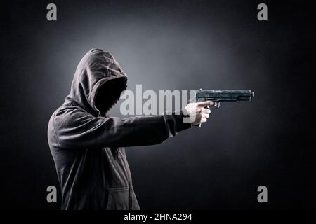 Uomo incappucciato con una pistola nel buio Foto Stock