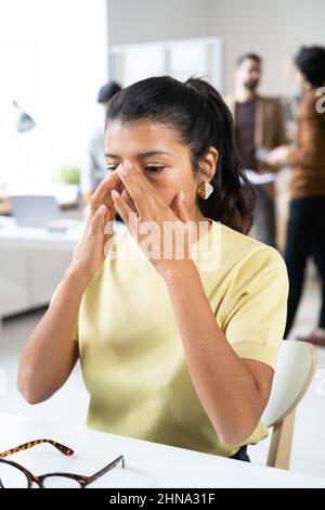 Triste donna d'affari che pulendo le lacrime dal suo viso mentre si siede al suo posto di lavoro in ufficio, lei che ha un brutto giorno al suo lavoro Foto Stock