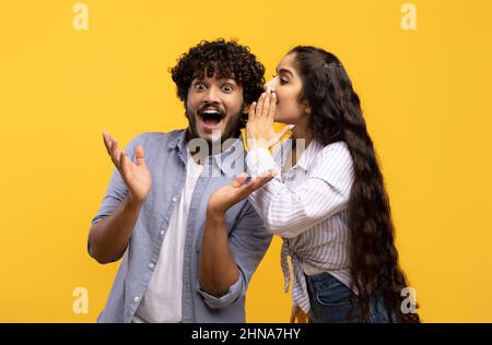Giovane donna indiana che condivide i segreti con il suo ragazzo eccitato, coppia millennial sussurrando i gossips l'uno all'altro Foto Stock