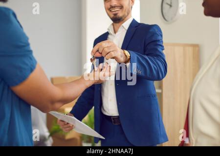 Il venditore domestico maschio, l'agente immobiliare o l'agente immobiliare dà le chiavi alla nuova sede alla coppia sposata giovane. Foto Stock