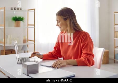 Giovane donna intelligente e di successo che lavora su un notebook seduto sul posto di lavoro in ufficio. Foto Stock