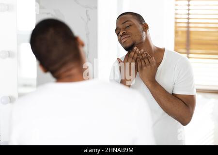 Problema dei capelli incarniti. Ritratto del Guy nero non rasato che tocca il collo con le setole Foto Stock