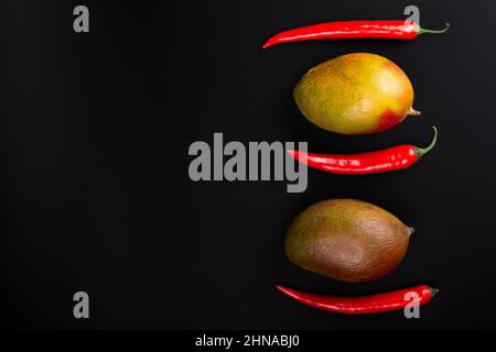 Manghi interi e peperoncini piccanti su sfondo nero. Banner Foto Stock