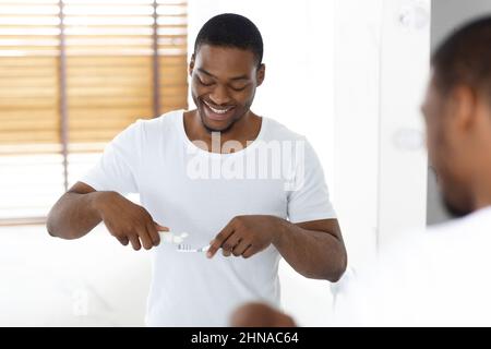 Bell'uomo nero applicazione dentifricio su spazzolino vicino specchio in bagno Foto Stock