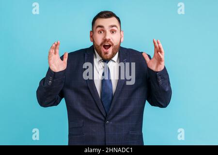 WOW, è incredibile. L'uomo sorpreso in stile ufficiale vestito fissando la macchina fotografica con la bocca ampiamente aperta e gli occhi grandi, sollevando le braccia in stupore. Studio interno girato isolato su sfondo blu. Foto Stock