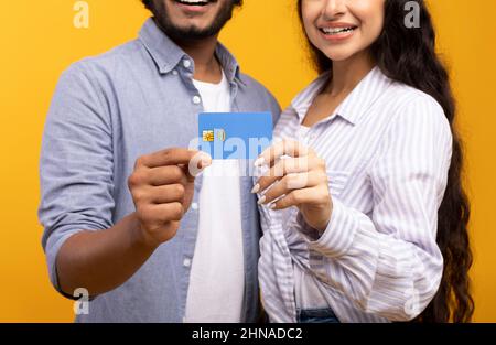 Vista ritagliata della coppia indiana che tiene la carta di credito su sfondo giallo studio, fuoco sulle mani Foto Stock