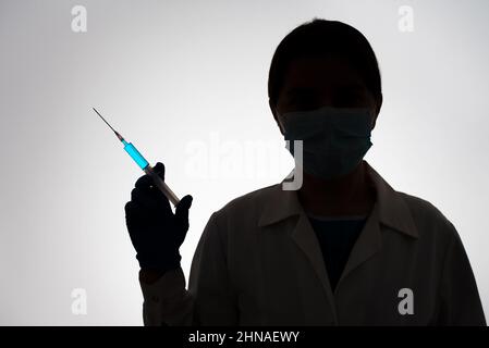 Silhouette di un medico con siringa riempita di liquido blu. Concetto di vaccinazione. Foto Stock