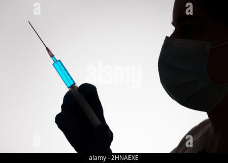 Silhouette di un medico con siringa riempita di liquido blu. Concetto di vaccinazione. Foto Stock