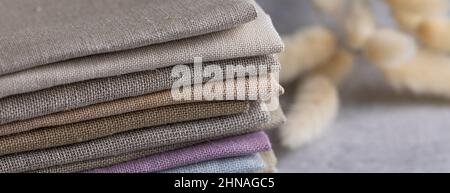 Un mucchio di quattro tessuti di lino naturale piegati colorati ecologicamente compatibili su sfondo grigio Foto Stock