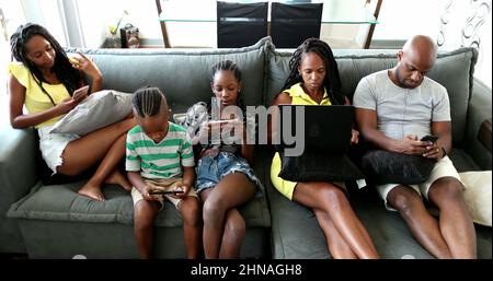 Casual famiglia africana rilassarsi a casa divano utilizzando la tecnologia. I genitori e i bambini neri che utilizzano i loro dispositivi tecnologici sono tutti bolle Foto Stock