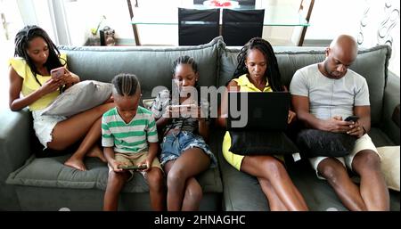 Casual famiglia africana rilassarsi a casa divano utilizzando la tecnologia. I genitori e i bambini neri che utilizzano i loro dispositivi tecnologici sono tutti bolle Foto Stock