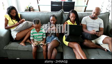 Casual famiglia africana rilassarsi a casa divano utilizzando la tecnologia. I genitori e i bambini neri che utilizzano i loro dispositivi tecnologici sono tutti bolle Foto Stock