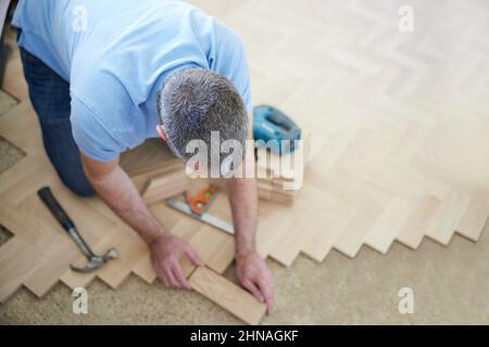 Vista dall'alto di Carpentiere o costruzione posa di nuovo legno blocco parquet pavimento in cucina a casa Foto Stock