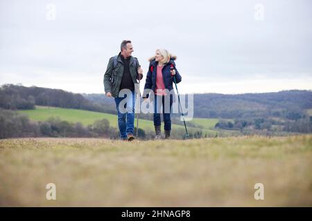 Coppie mature camminano attraverso la campagna autunnale o invernale utilizzando poli escursionistici Foto Stock