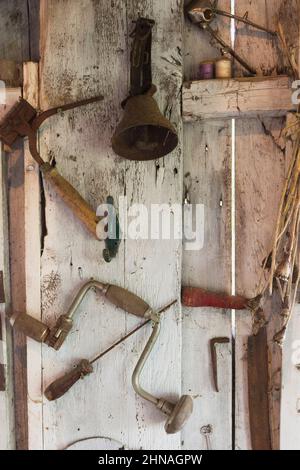 Attrezzi e oggetti antichi appesi a parete all'interno di una vecchia cabina rustica in legno. Foto Stock