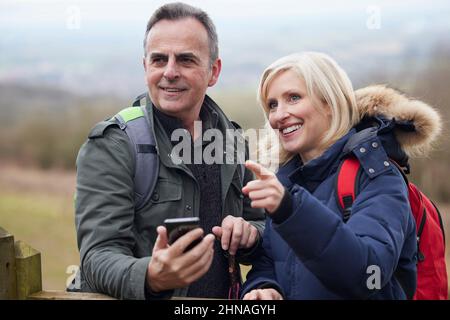 Una coppia matura in pensione cammina in autunno o in inverno nella campagna utilizzando la mappa o l'app di navigazione sul telefono cellulare Foto Stock