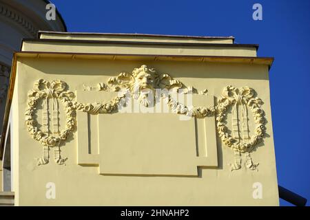 Opatija, Croazia, 22 gennaio 2022. La faccia della gargoyle e' decorata con corone di fiori su una facciata dell'edificio gialla Foto Stock