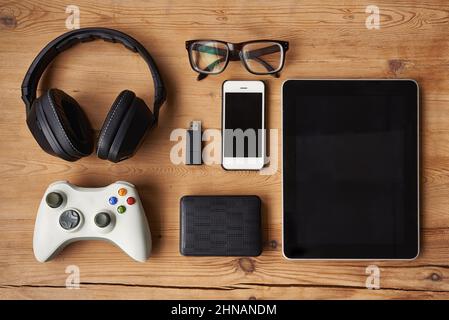 Tutto ciò di cui hai bisogno in una giornata trascorsa. Scatto ad angolo elevato della tecnologia wireless su un tavolo in legno. Foto Stock